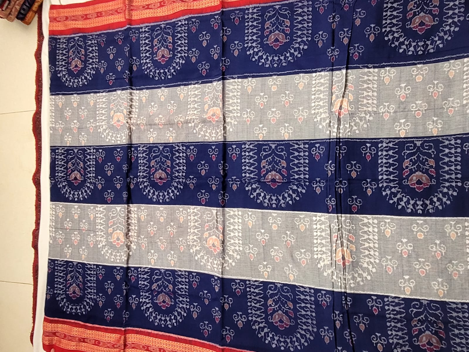 A blue and white Sambalpuri cotton saree featuring a unique body pattern with trees and small figures, complemented by a stylish pallu design.