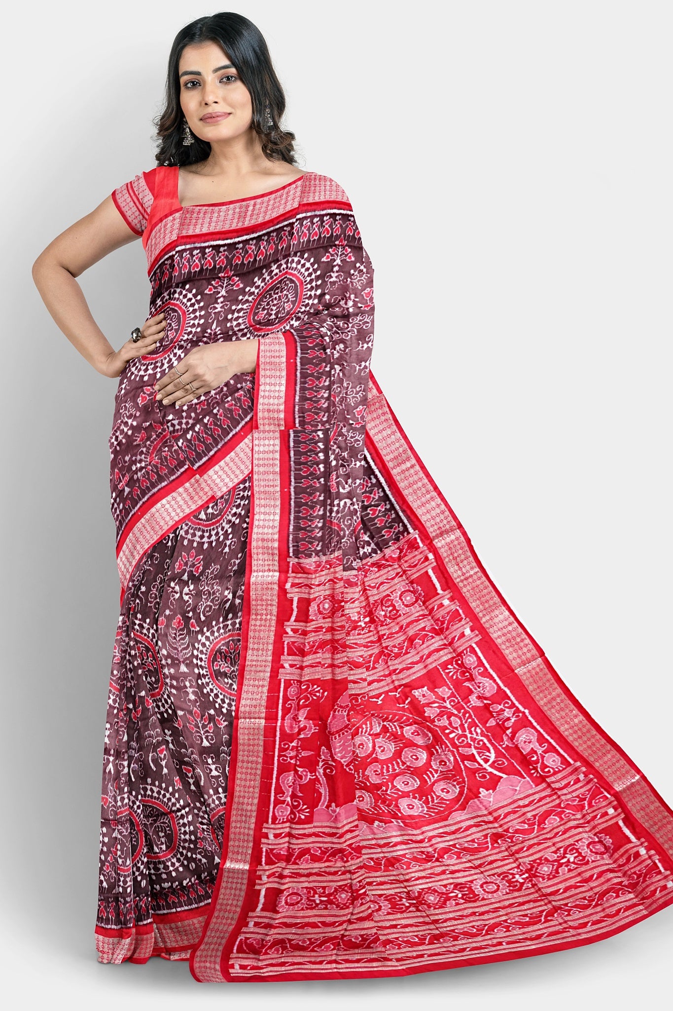 A coffee and red pure pata saree featuring round flowers and Adivasi patterns on the body, with peacock and floral tree pallu design.