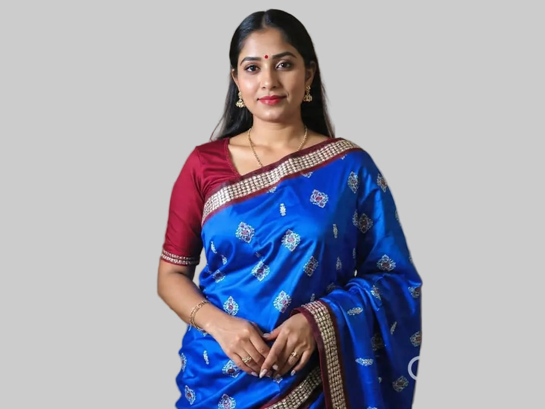 Woman wearing a blue saree with a red blouse against a wooden paneled wall.