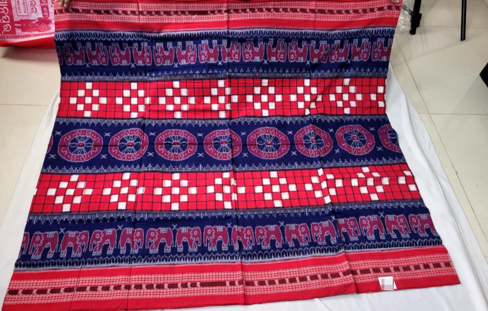 This blue and red Sambalpuri cotton saree features an elegant body pattern of elephants and Pasapali design, with a floral pallu design.